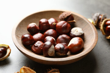 Horse chestnuts in wooden bowl on grey table, closeup