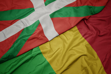 waving colorful flag of mali and national flag of basque country.