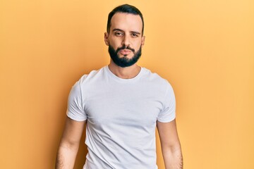 Young man with beard wearing casual white t shirt with serious expression on face. simple and natural looking at the camera.