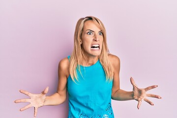 Beautiful blonde woman wearing casual clothes crazy and mad shouting and yelling with aggressive...