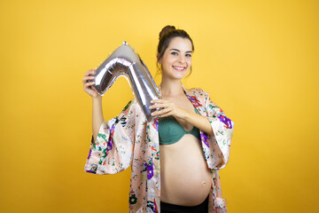 Young beautiful woman pregnant expecting baby wearing pajama over isolated yellow background holding a number seven balloon. Celebration concept