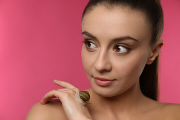 Beautiful young woman with snail on her hand against pink background