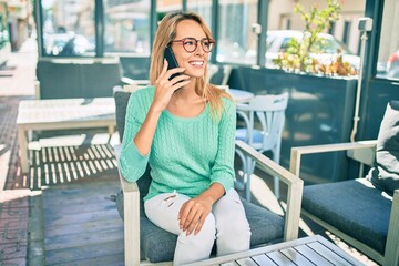 Young blonde woman smiling happy talking on the smartphone sitting at the coffee shop terrace.