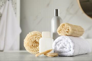 Fototapeta na wymiar Natural loofah sponges, towel and cosmetic products on table in bathroom