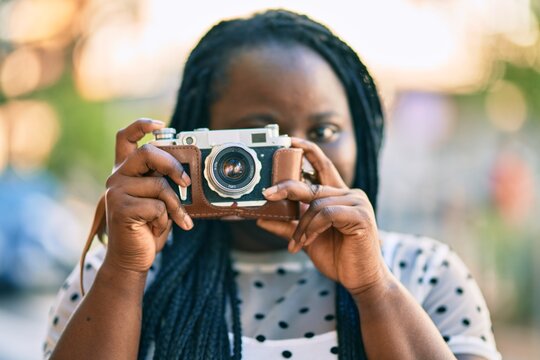 Young african american tourist woman smiling happy using vintage camera at the city.