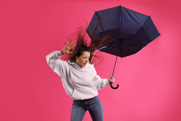 Emotional woman with umbrella caught in gust of wind on pink background