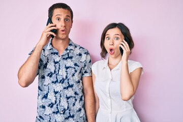 Beautiful couple having conversation talking on the smartphone scared and amazed with open mouth for surprise, disbelief face