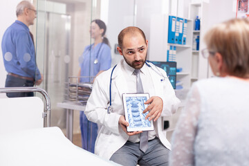 Obraz premium Doctor discussing about bones disease with senior woman during medical examination in hospital. Medical therapist showing and talking about x-ray with patient during consultation.