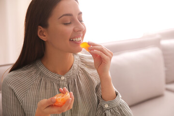 Happy woman eating tasty fresh tangerine indoors