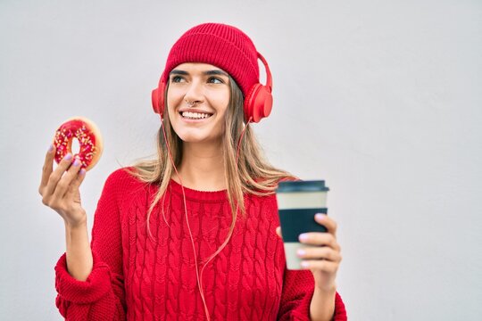 Young hispanic woman having breakfast using headphones at the city.