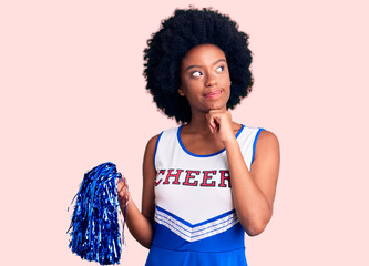 Young african american woman wearing cheerleader uniform holding pompom with hand on chin thinking about question, pensive expression. smiling and thoughtful face. doubt concept.