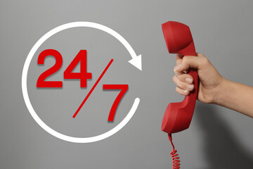 24/7 hotline service. Woman holding handset on grey background, closeup