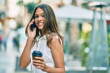 Beautiful latin teenager girl talking on the smartphone and drinking coffee at the city.