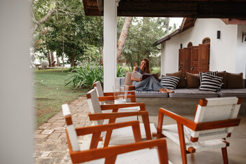 Cozy home. Pretty young woman is reading book/ journal on beautiful terrace of her house