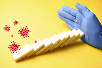 Doctor stopping domino effect on yellow background, closeup. Prevent spreading of coronavirus