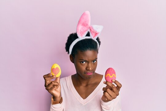 Young african american girl wearing cute easter bunny ears holding painted eggs skeptic and nervous, frowning upset because of problem. negative person.