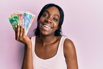 Young african american woman holding south african rand banknotes looking positive and happy...