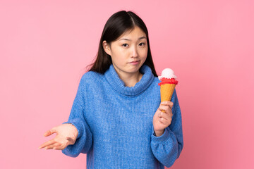 Young asian woman with a cornet ice cream isolated on pink background making doubts gesture while lifting the shoulders