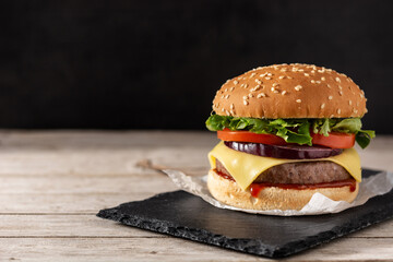Cheeseburger with beef,tomato, lettuce and onion on wooden table. Copy space
