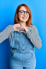 Obraz na płótnie Canvas Beautiful redhead woman wearing casual clothes and glasses smiling in love doing heart symbol shape with hands. romantic concept.