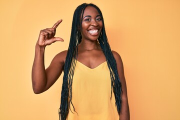 African american woman with braids wearing casual clothes smiling and confident gesturing with hand doing small size sign with fingers looking and the camera. measure concept.