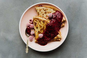 Pancake with jam and raspberries on a plate close-up.