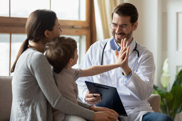 Happy male doctor have fun cheer support small 7s boy patient at visit to clinic with mom. Caring...