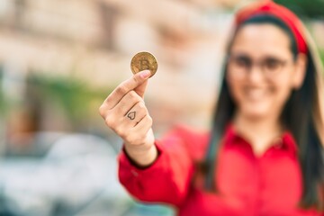 Young hispanic woman smiling happy holding bitcoin at the city.