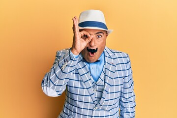 Mature middle east man with mustache wearing vintage and elegant fashion style doing ok gesture shocked with surprised face, eye looking through fingers. unbelieving expression.