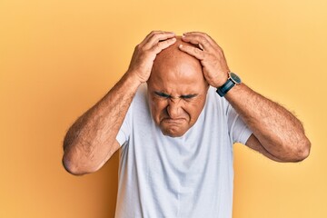 Mature middle east man wearing casual white tshirt suffering from headache desperate and stressed because pain and migraine. hands on head.