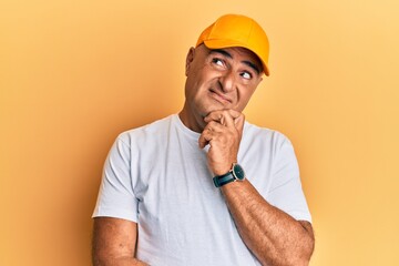 Mature middle east man with mustache wearing casual white tshirt and yellow cap thinking concentrated about doubt with finger on chin and looking up wondering