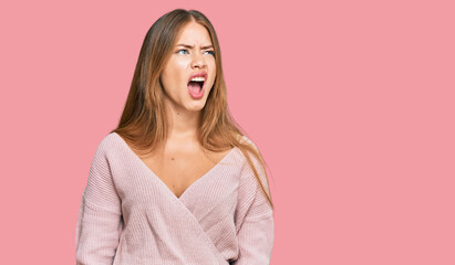 Fototapeta premium Beautiful blonde woman wearing casual winter pink sweater angry and mad screaming frustrated and furious, shouting with anger. rage and aggressive concept.