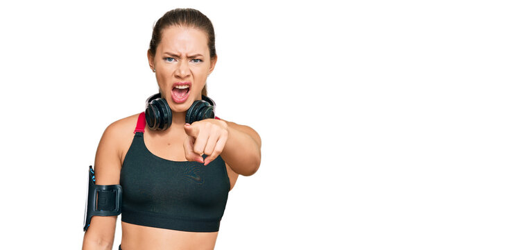 Beautiful blonde woman wearing gym clothes and using headphones pointing displeased and frustrated to the camera, angry and furious with you