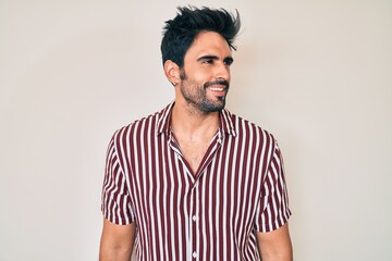 Handsome hispanic man with beard wearing casual clothes looking away to side with smile on face,...