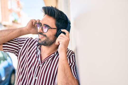 Young handsome hispanic man with beard smiling happy outdoors wearing headphones listening to music