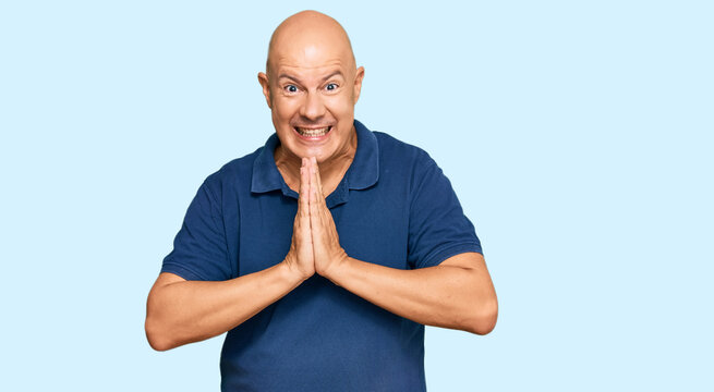 Middle age bald man wearing casual clothes praying with hands together asking for forgiveness smiling confident.