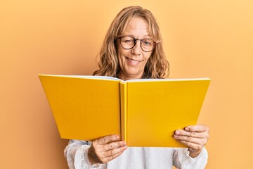 Middle age blonde woman reading a book wearing glasses winking looking at the camera with sexy...