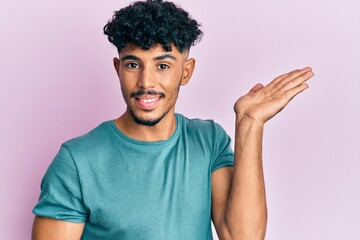 Fototapeta na wymiar Young arab handsome man wearing casual clothes smiling cheerful presenting and pointing with palm of hand looking at the camera.
