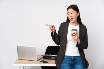 Business asian woman in her workplace isolated on white background pointing finger to the side and presenting a product