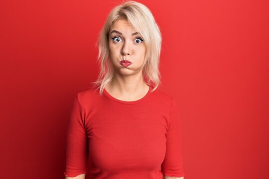 Young blonde girl wearing casual clothes puffing cheeks with funny face. mouth inflated with air, crazy expression.