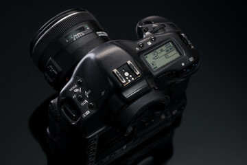 A used professional SLR camera with a lens sits on a glass table with a reflection. Advertising...