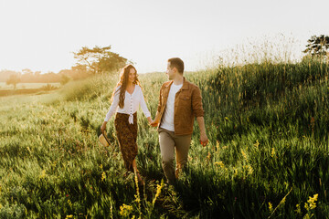 Beautiful young woman and a man walk, hug and kiss in nature at sunset.