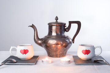 Teapot and two cups with painted hearts and burning candles.. Romantic tea time or breakfast. Concept of love and Valentines day   