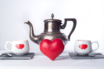 Teapot and two cups with hearts painted on them., and a red love heart in the middle. Romantic tea time or breakfast. Concept of love and Valentines day 