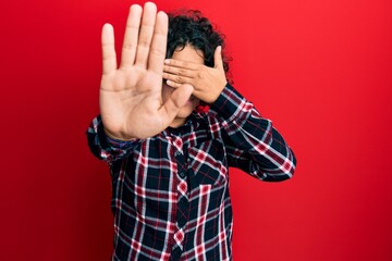 Young hispanic woman with curly hair wearing casual clothes and glasses covering eyes with hands and doing stop gesture with sad and fear expression. embarrassed and negative concept.