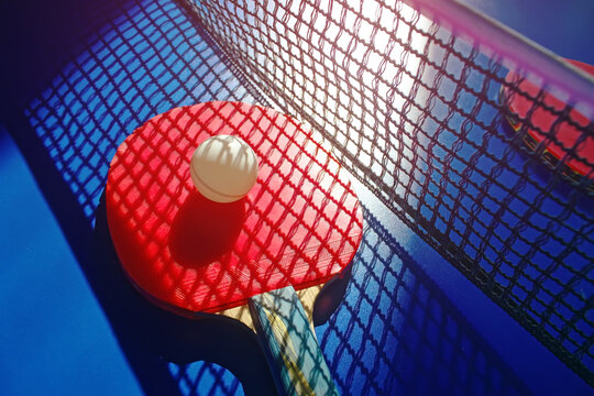 A Red Table Tennis Racket And A White Ball Lie On The Surface Of The Table Next To The Net. Sports Game And Active Recreation.