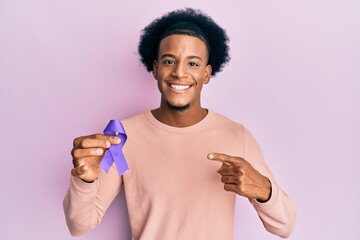 African american man with afro hair holding awareness purple ribbon smiling happy pointing with...