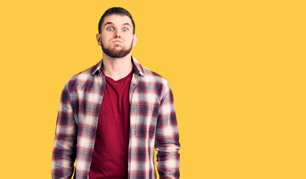Young handsome man wearing casual shirt puffing cheeks with funny face. mouth inflated with air, crazy expression.