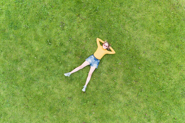Young girl lies on the grass. Fresh natural summer concept. View from air.