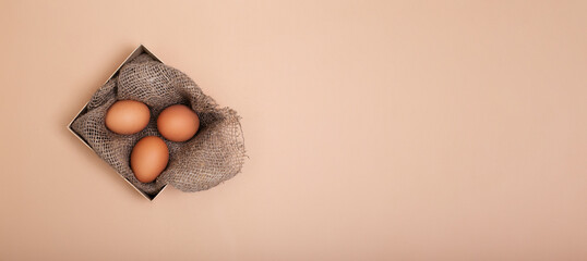 Easter eggs in sustainable box with natural canva burlap cloth on beige background with copy space. Zero waste holiday banner. Eco-friendly egg advertising card. Top view.